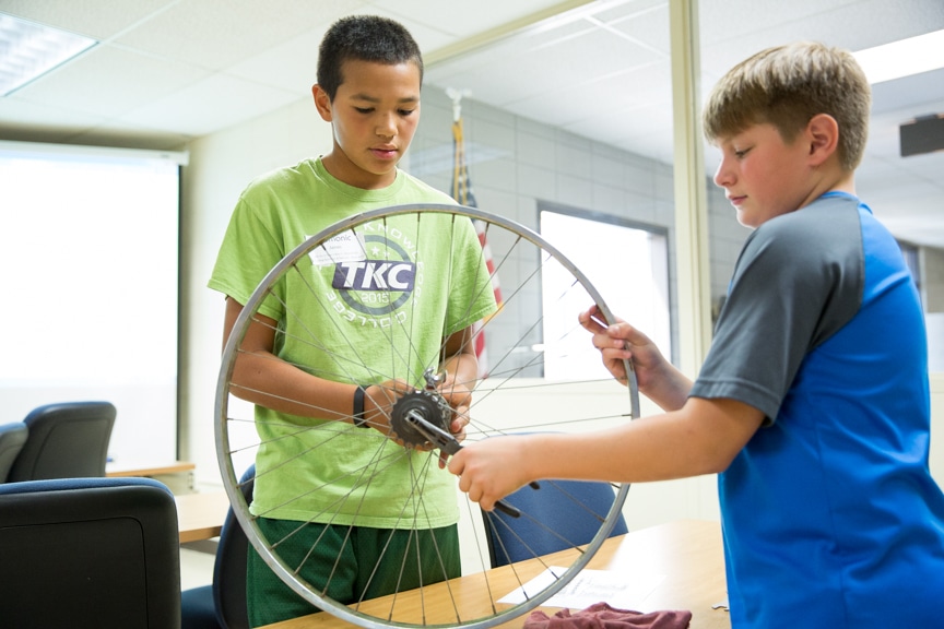 Two boys working on bicycle wheel at Tech Knowledge College event