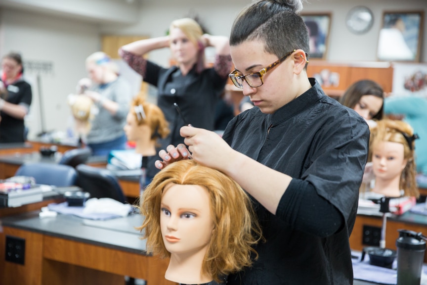 female cosmetology student parting mannequin hair