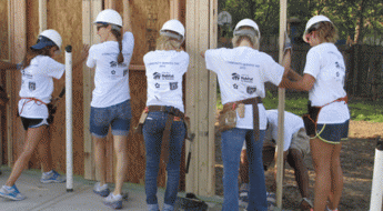 Females working on setting up a house frame