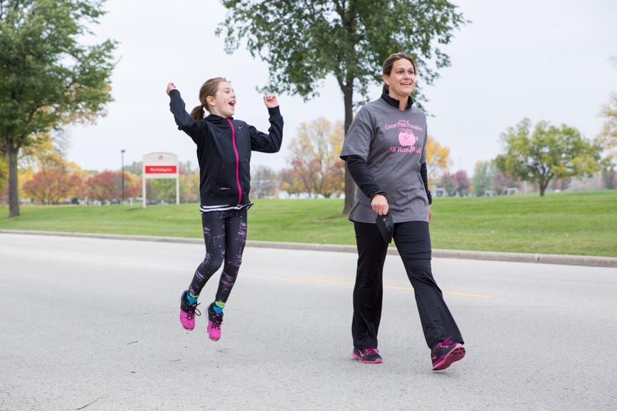 child jumps and smiles next to woman at pink pumpkin walk