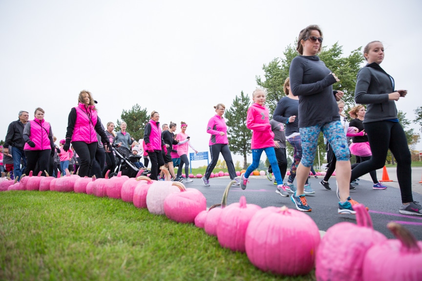 participants run alongside row of pink pumpkins