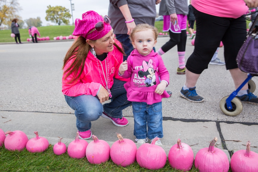 woman and child look at pink pumpkins lining street