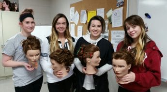 Four female Cosmetology students holding mannequin hair styles