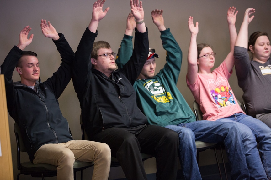 group of hypnotized students lean back in chairs as if riding roller coaster