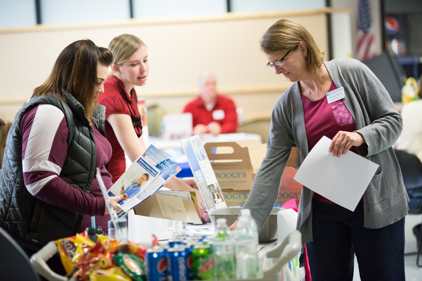 staff member reaches for item on table at healthcare career fair