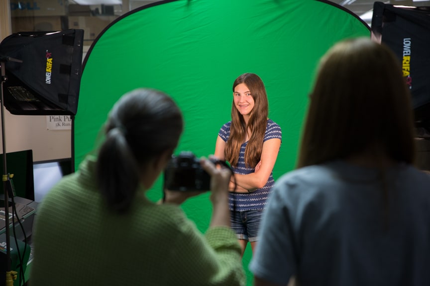 Girl poses in front of green screen during photography activity at Moraine Park summer camp