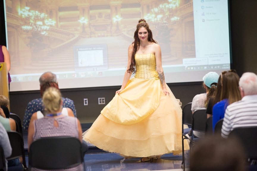 Model dressed as Beauty and the Beast character walks down runway in yellow dress at MPTC fashion show