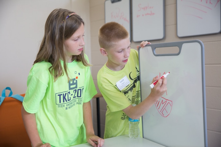 Two students draw logos on whiteboard during business management activity at Moraine Park summer camp
