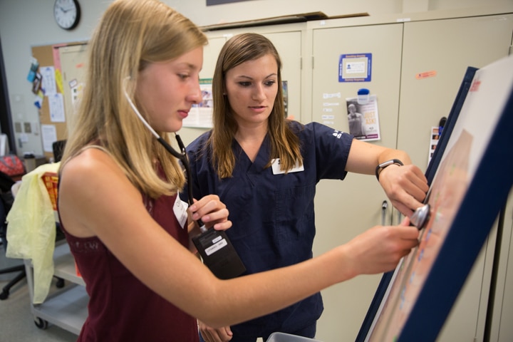 Instructor helps girl use stethoscope to hear simulated chest sounds at Moraine Park Tech Knowledge College