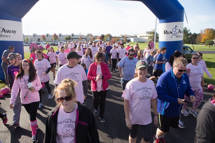 large group of people take off from start line of pink pumpkin run